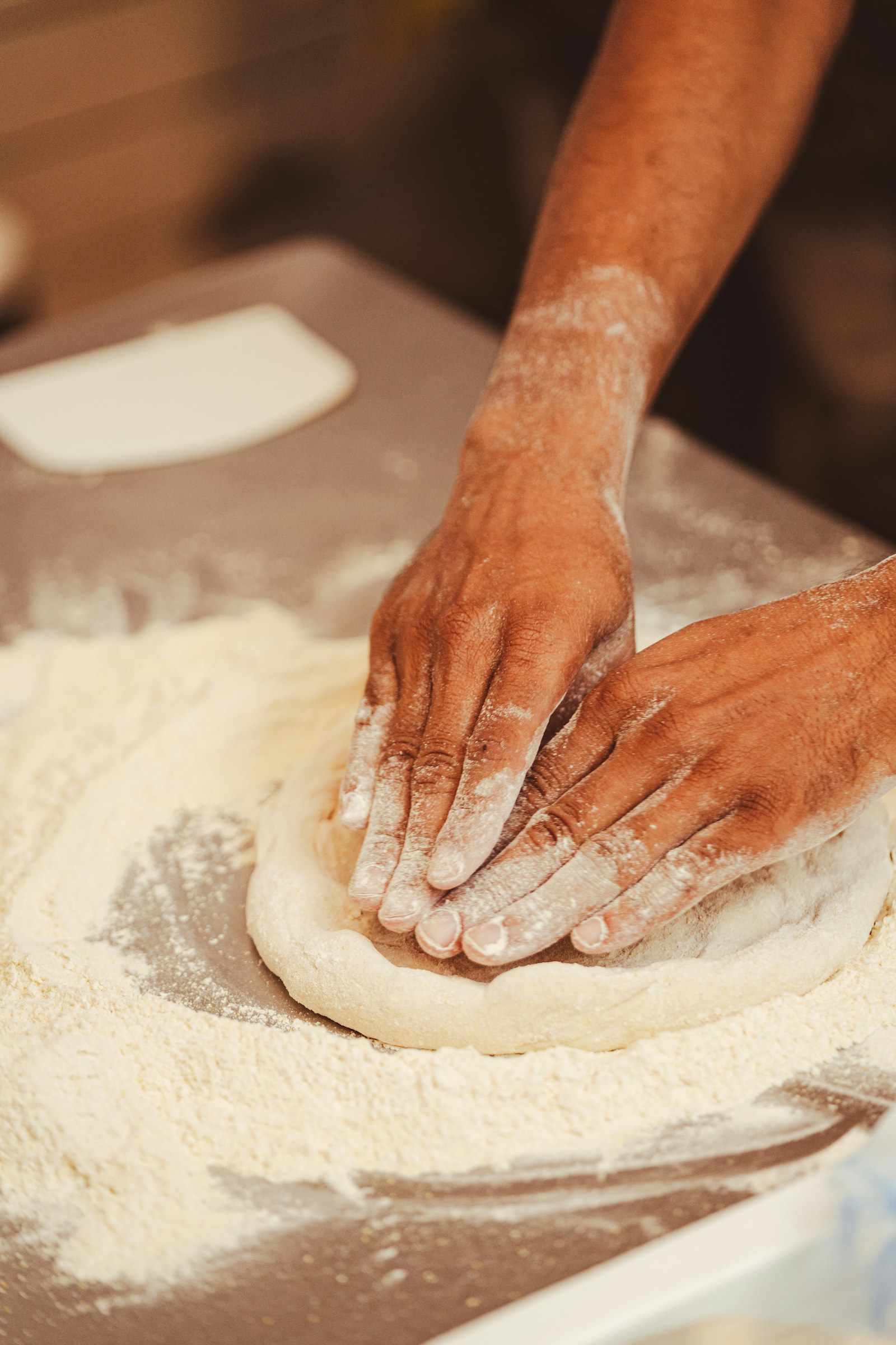 Hands shaping pizza dough on a floured worktop